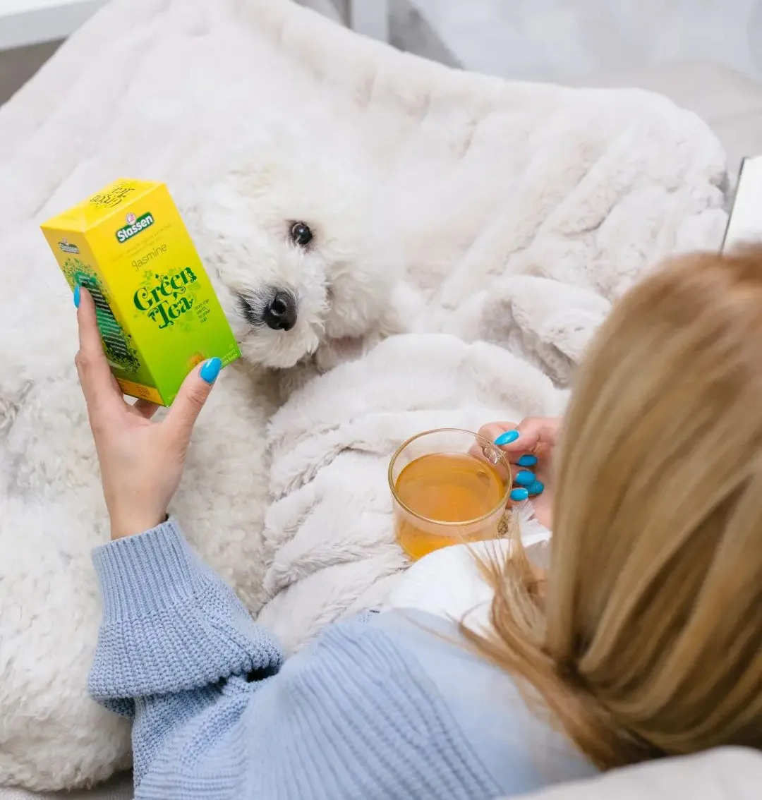 Person holding Stassen Jasmine Green Tea and a glass of freshly brewed tea
